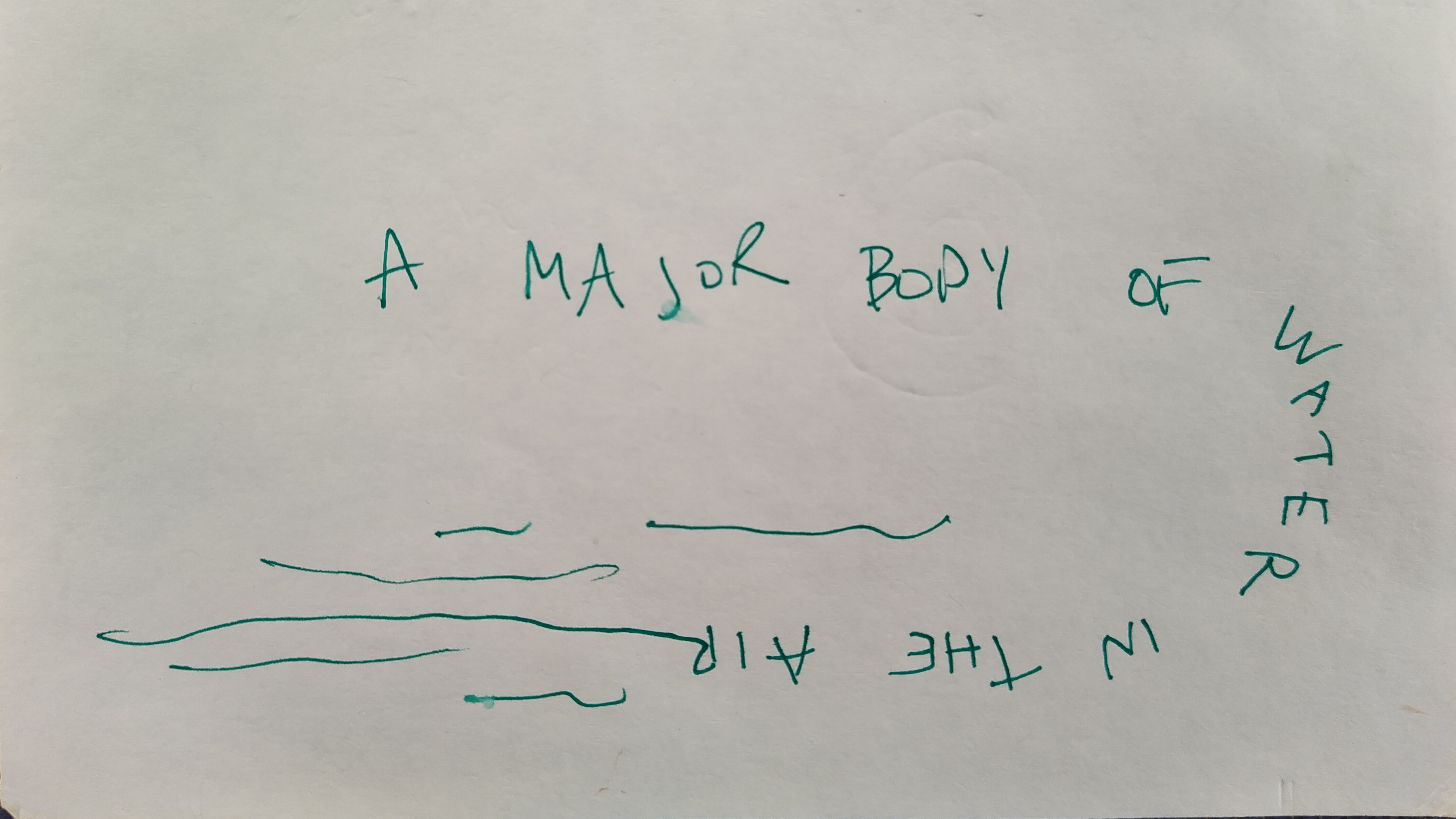 An index card on which the wirds "a major body of water in the air" are written in a curved fashion and truning in to horizontal squiggily lines intended to depict water and or air.