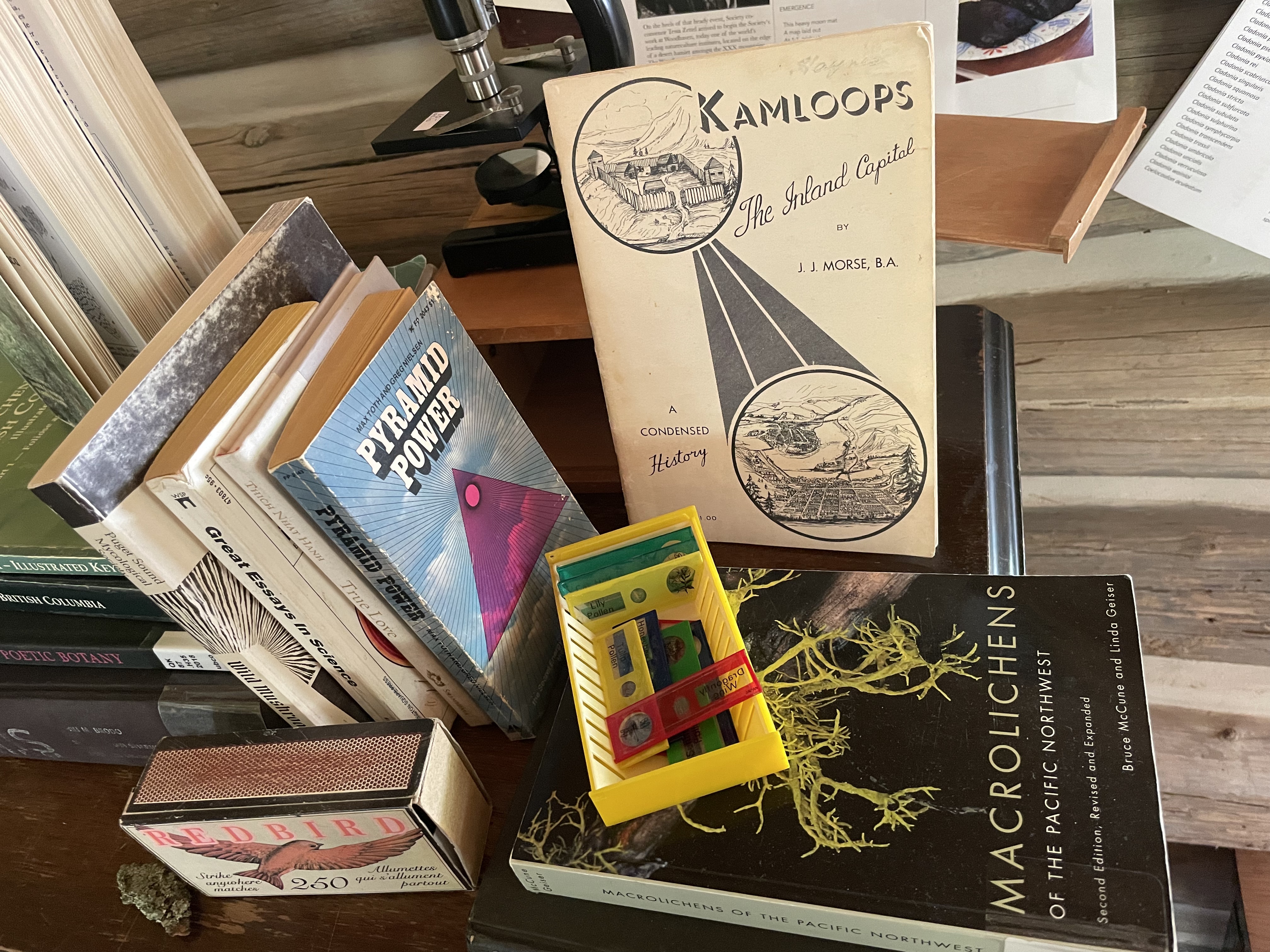A pile of books, instruments, matches. The main texts have the titles "Macrolichens of the Pacific Northwest" "Pyramid Power" and "Kamloops: The Inland Capital"