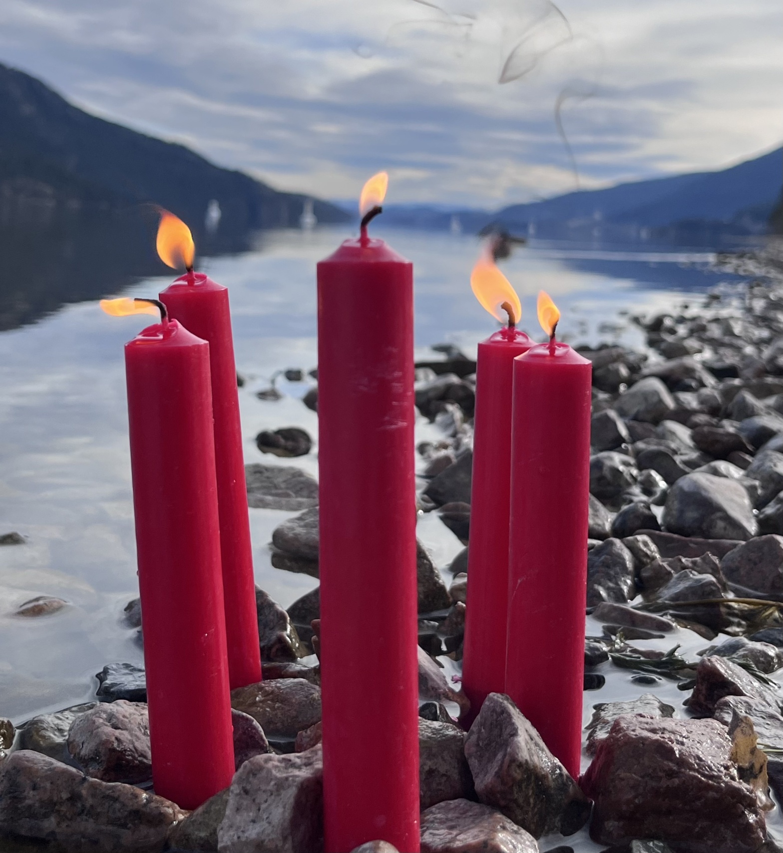 the flames from five lit red candles flicker, against a backdrop of rocks and water